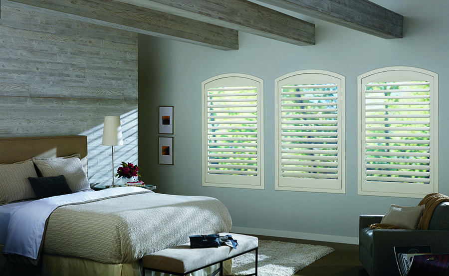 Arched windows with interior shutters in bedroom.