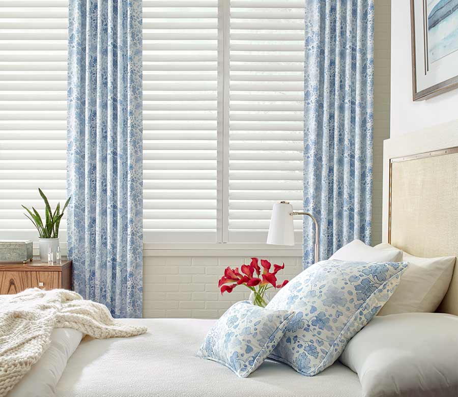 coastal guest bedroom white plantation shutters framed by blue floral curtains in san antonio, TX