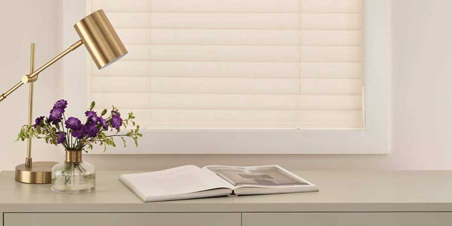 white aria soft blinds on an office window with a desk and gold lamp